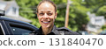 A friendly female police officer stands next to her patrol car, smiling at the camera as the sun sets behind her, showcasing a warm, community-focused moment, banner 131840470