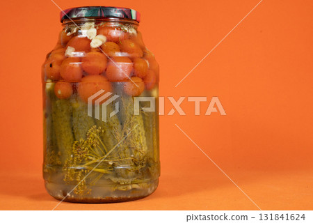 Homemade pickled canned tomatoes and cucumbers in glass jar on orange background 131841624