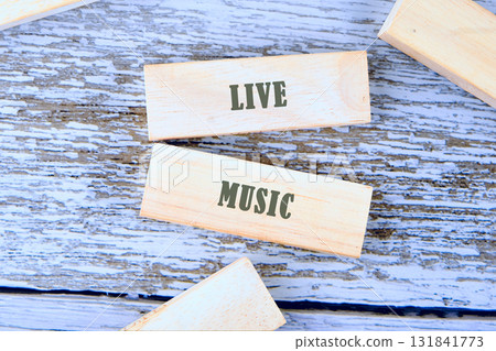 Wooden blocks are arranged on a rustic, painted surface. Two blocks display the words LIVE and MUSIC in a simple, bold font, suggesting a musical performance Wooden blocks are arranged on a rustic, painted surface. Two blocks display the words LIVE and MUSIC in a simple, bold font, suggesting a musical performance 131841773