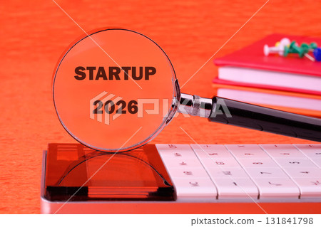 A calculator and books are positioned on a desk as a magnifying glass examines the concept of Startup 2026, implying research and financial planning for a business A calculator and books are positioned on a desk as a magnifying glass examines the concept of Startup 2026, implying research and financial planning for a business 131841798
