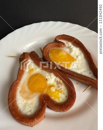 A close-up of two Frankfurt sausages, cut into hearts and fried with eggs in vegetable oil. Cooking delicious food at home. 131842492