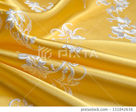 Luxurious silk fabric with a dazzling golden drape and striking white embroidery 131842638
