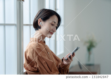 操作智能手機的婦女在窗口旁邊 操作智能手機的婦女在窗口旁邊 131842847