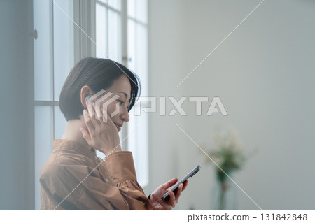 操作智能手機的婦女在窗口旁邊 操作智能手機的婦女在窗口旁邊 131842848