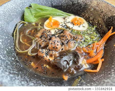 Delicious ramen noodle soup with chicken, boiled egg, and green onions served in a dark ceramic bowl. Traditional Asian Japanese food concept, top view 131842918