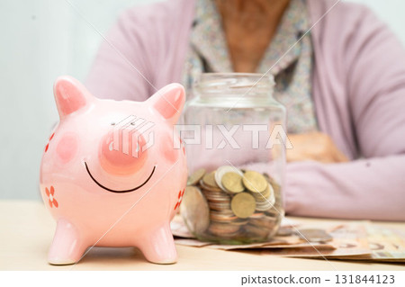 Retired elderly woman counting coins money with piggy bank and worry about monthly expenses and treatment fee payment. 131844123