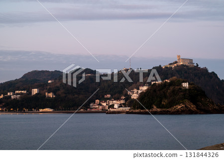 Resort hotels lined up along Concha Beach in San Sebastian, street lights and buildings on the hillside in the morning glow Resort hotels lined up along Concha Beach in San Sebastian, street lights and buildings on the hillside in the morning glow 131844326