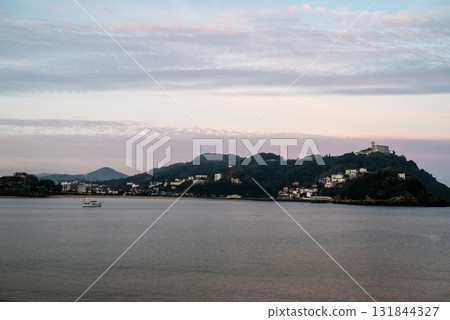 Resort hotels lined up along Concha Beach in San Sebastian, street lights and buildings on the hillside in the morning glow Resort hotels lined up along Concha Beach in San Sebastian, street lights and buildings on the hillside in the morning glow 131844327