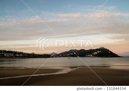 The shallow sandy beach of Concha Beach in San Sebastian at sunrise and the buildings lining the hillside in the distance The shallow sandy beach of Concha Beach in San Sebastian at sunrise and the buildings lining the hillside in the distance 131844334
