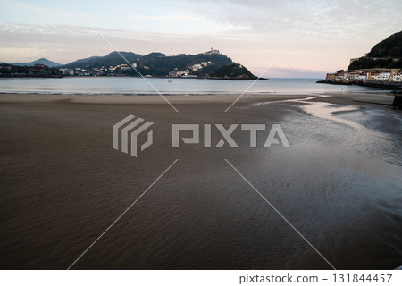 The shallow sandy beach of Concha Beach in San Sebastian at sunrise and the buildings lining the hillside in the distance The shallow sandy beach of Concha Beach in San Sebastian at sunrise and the buildings lining the hillside in the distance 131844457