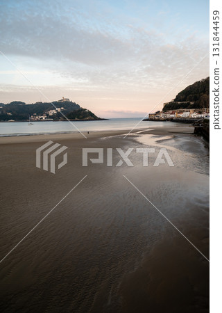 The shallow sandy beach of Concha Beach in San Sebastian at sunrise and the buildings lining the hillside in the distance 131844459