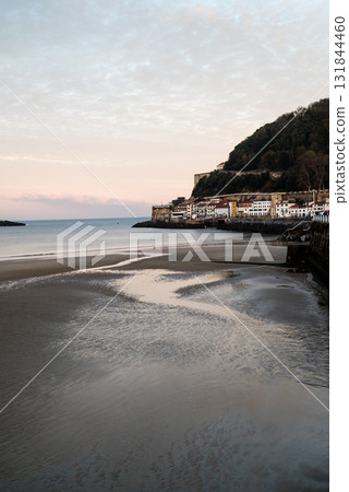 日出時分，聖塞巴斯蒂安孔查海灘的淺沙灘和遠處山坡上的建築物 131844460