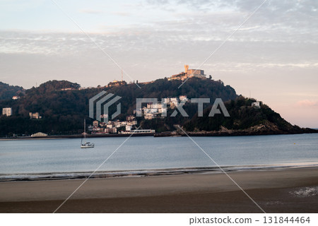 The shallow sandy beach of Concha Beach in San Sebastian at sunrise and the buildings lining the hillside in the distance The shallow sandy beach of Concha Beach in San Sebastian at sunrise and the buildings lining the hillside in the distance 131844464