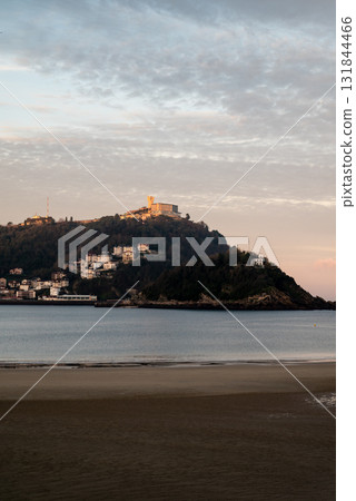The shallow sandy beach of Concha Beach in San Sebastian at sunrise and the buildings lining the hillside in the distance 131844466