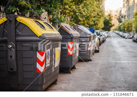 Recycling containers lined up along a quiet street in Rome, Italy, with yellow and brown lids for sorted waste collection promoting sustainable urban waste management. Recycling containers lined up along a quiet street in Rome, Italy, with yellow and brown lids for sorted waste collection promoting sustainable urban waste management. 131846671