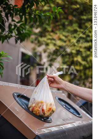 Man throwing sorted organic waste in a compost bin on a street in Rome, Italy, demonstrating eco-friendly recycling and urban waste management. Man throwing sorted organic waste in a compost bin on a street in Rome, Italy, demonstrating eco-friendly recycling and urban waste management. 131846724