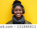 A smiling African American woman with headphones on, set against a vibrant yellow background, captured in clean minimalism, evoking the concept of music enjoyment or learning 131846811
