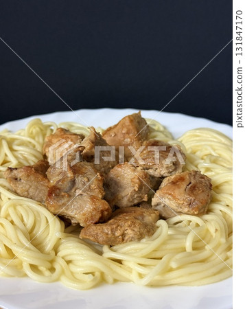 Close-up shot of spaghetti with fried pork pieces on a white plate. Cooking delicious food at home. Close-up shot of spaghetti with fried pork pieces on a white plate. Cooking delicious food at home. 131847170