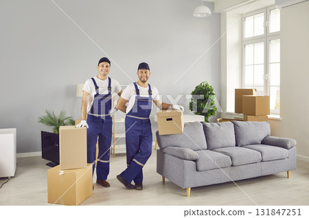 Portrait of two friendly workers of moving and delivery company who transport cardboard boxes. 131847251
