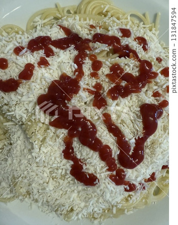 Close-up of spaghetti on a white plate topped with grated salted ricotta and drizzled with ketchup. Cooking delicious food at home. Close-up of spaghetti on a white plate topped with grated salted ricotta and drizzled with ketchup. Cooking delicious food at home. 131847594