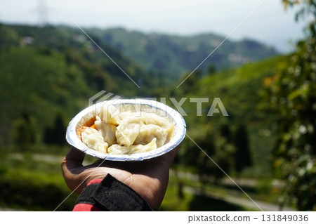 Close up of Steamed Momos Held Against a Blurred Panoramic Green Mountain Landscape Close up of Steamed Momos Held Against a Blurred Panoramic Green Mountain Landscape 131849036