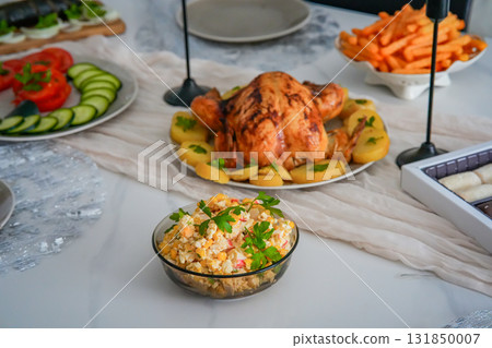Close-up side view of a festive holiday table featuring roasted chicken, crispy fries, and fresh vegetables. Cozy Christmas, Thanksgiving, or New Year family celebration with colorful and appetizing 131850007