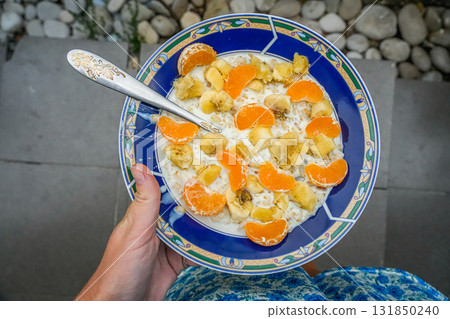 Hand holding plate with oatmeal, banana and mandarin Hand holding plate with oatmeal, banana and mandarin 131850240