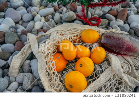 Mandarins in net and red lemonade bottle on pebbly beach 131850241