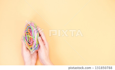 Hands Holding Colorful Rubber Bands on a Beige Background, Creative and Playful Concept 131850788