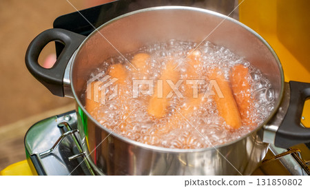 Boiling sausages in a stainless steel pot on a stove, surrounded by bubbling water, showcasing the cooking process and vibrant colors of vegetables 131850802