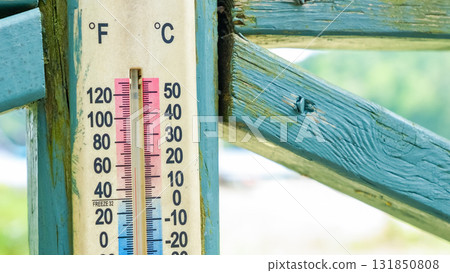 Close-up of a vintage thermometer mounted on a weathered wooden fence, showcasing temperature readings in Fahrenheit and Celsius for environmental context 131850808