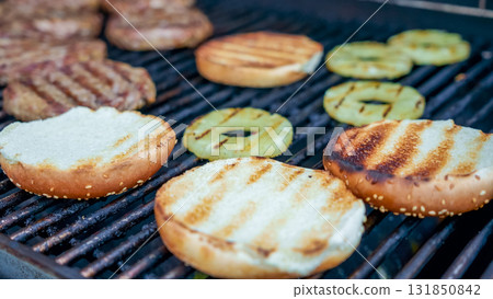 Grilled burger patties and toasted sesame buns with pineapple slices on barbecue grill, showcasing summer cooking and outdoor dining experience 131850842