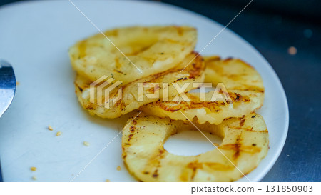 Grilled pineapple slices arranged on a white plate, showcasing caramelized edges and juicy texture, perfect for summer recipes and tropical dishes Grilled pineapple slices arranged on a white plate, showcasing caramelized edges and juicy texture, perfect for summer recipes and tropical dishes 131850903