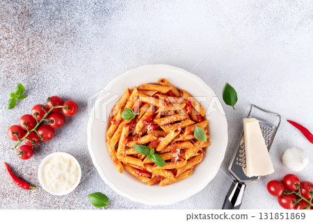 Classic Italian pasta arrabbiata with tomato sauce, chili pepper and parmesan on grey background. Top view Classic Italian pasta arrabbiata with tomato sauce, chili pepper and parmesan on grey background. Top view 131851869