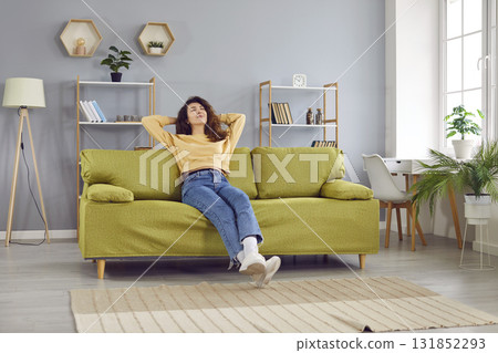 Happy relaxed young woman sitting on comfortable sofa Happy relaxed young woman sitting on comfortable sofa 131852293
