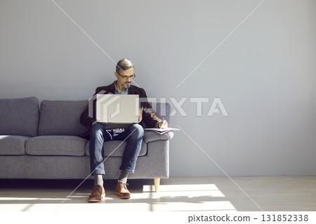 Businesslike, handsome, brutal man is sitting on the couch with laptop and making notes in notebook. Businesslike, handsome, brutal man is sitting on the couch with laptop and making notes in notebook. 131852338