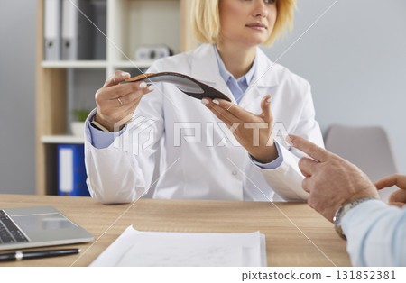 Young woman doctor gives comfortable orthotic medical shoe insole to senior man patient 131852381