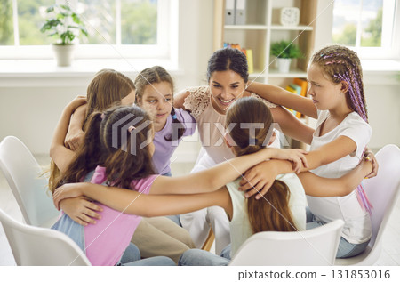Girls sitting in a circle and hugging with teacher or psychologist woman during therapy session. Girls sitting in a circle and hugging with teacher or psychologist woman during therapy session. 131853016