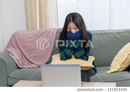 Happy teen woman at home using laptop, enjoys online work, customer shop browsing, relaxing with computer on comfortable sofa, smiling, covering mouth with striped sleeve. Happy teen woman at home using laptop, enjoys online work, customer shop browsing, relaxing with computer on comfortable sofa, smiling, covering mouth with striped sleeve. 131853340