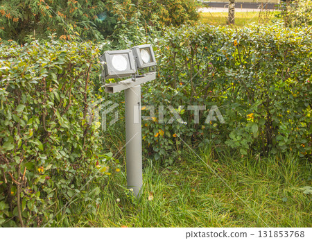 Two LED floodlights on a garden post, gray metal among green foliage Two LED floodlights on a garden post, gray metal among green foliage 131853768