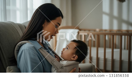 Young asian mother and baby boy bonding in carrier at home with loving gaze Young asian mother and baby boy bonding in carrier at home with loving gaze 131856338