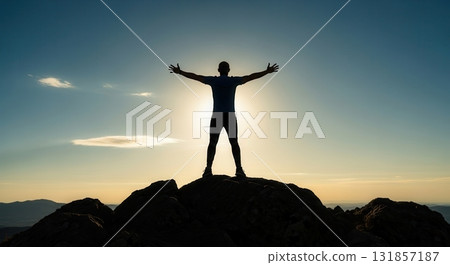 Silhouette of a man with outstretched arms on a mountain peak at sunset, celebrating freedom. 131857187