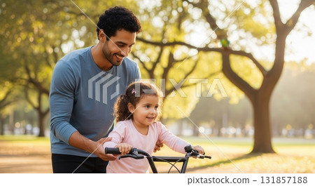 Happy father teaching his smiling daughter to ride a bicycle in a sunny park 131857188