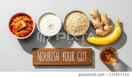 Flat lay of gut healthy ingredients, kimchi, yogurt, oats, ginger, banana, kombucha, and nourish your gut sign 131857214