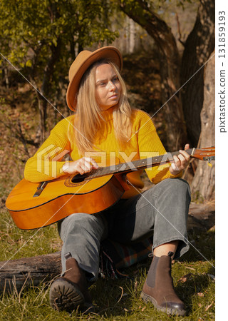 Blonde woman playing string guitar outdoors in autumn forest. Concept of sound therapy, mental health and wellness rituals. Calmness tranquility audio-sensory practices. Aura farming energy Blonde woman playing string guitar outdoors in autumn forest. Concept of sound therapy, mental health and wellness rituals. Calmness tranquility audio-sensory practices. Aura farming energy 131859193