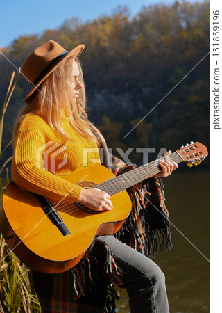 Blonde woman playing string guitar outdoors in autumn forest. Concept of sound therapy, mental health and wellness rituals. Calmness tranquility audio-sensory practices. Aura farming energy Blonde woman playing string guitar outdoors in autumn forest. Concept of sound therapy, mental health and wellness rituals. Calmness tranquility audio-sensory practices. Aura farming energy 131859196