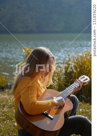 Blonde woman playing string guitar outdoors in autumn forest. Concept of sound therapy, mental health and wellness rituals. Calmness tranquility audio-sensory practices. Aura farming energy Blonde woman playing string guitar outdoors in autumn forest. Concept of sound therapy, mental health and wellness rituals. Calmness tranquility audio-sensory practices. Aura farming energy 131859220