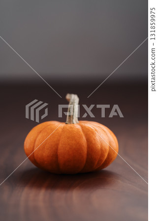 Small orange pumpkin on black walnut table with white wall background 131859975