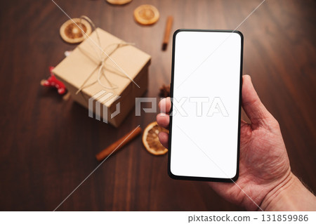 Man hand hold smarthone with white screen with christmas decorations on background Man hand hold smarthone with white screen with christmas decorations on background 131859986