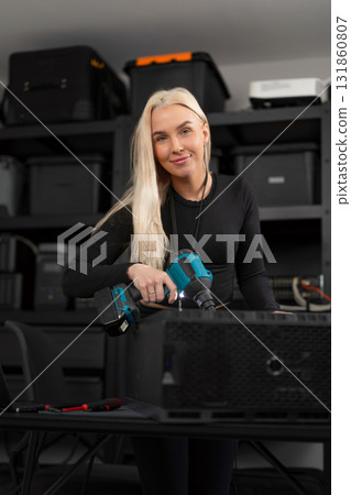 Female IT technician in her 30s repairs and clean a computer with a dust blower in a modern tech workshop 131860807